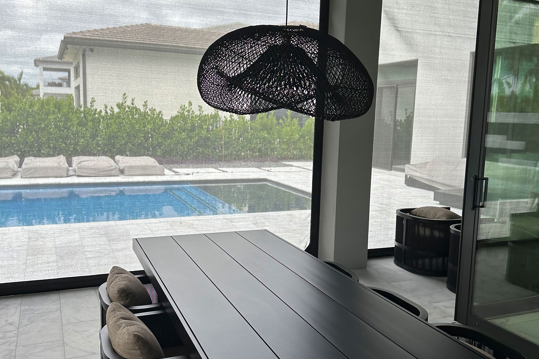 View of a pool through lowered fabric hurricane screens from inside a Boca Raton lanai