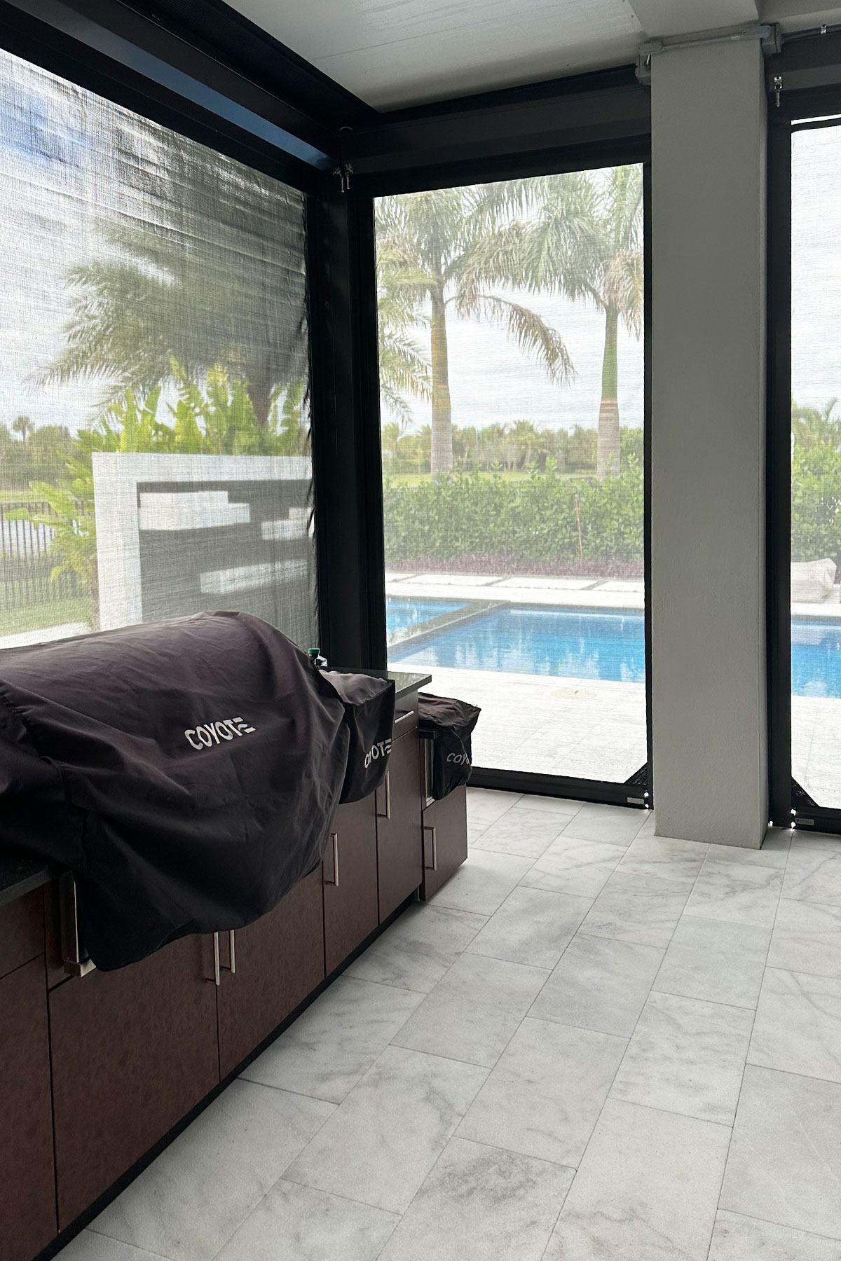 Outdoor grill protected behind fabric roll-down screens on a lanai